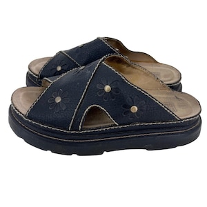May include: A pair of dark navy blue slide sandals featuring a textured leather upper with embossed daisy flower patterns and small metallic studs at the center of each flower. The sandals have a thick, dark navy blue platform sole and light stitching.