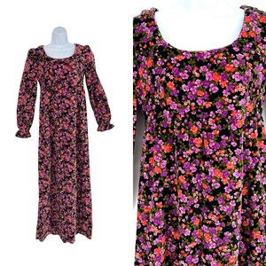 May include: A long-sleeved, floor-length dress with a scoop neckline. The dress features a black background covered in a floral pattern of purple, pink, and orange flowers. The sleeves end in ruffled cuffs. The dress is displayed on a white mannequin.