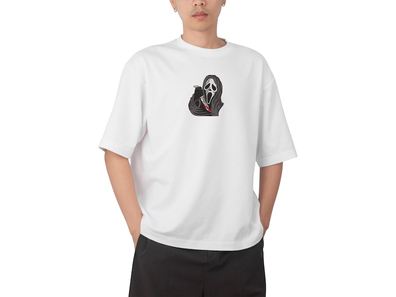 May include: White t-shirt with a black and red graphic of the Ghostface mask holding a bloody knife. The design is centered. The shirt has short sleeves and a relaxed fit.
