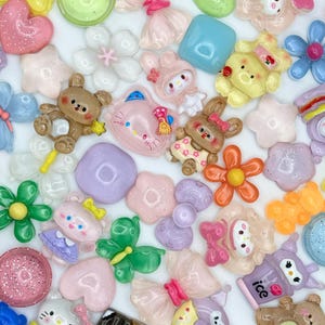 Könnte beinhalten: Sortiment an bunten Harz-Anhängern mit verschiedenen Designs, darunter Tiere, Blumen, Herzen und Essen. Die Anhänger sind aus klarem Harz mit Glitzer und anderen Verzierungen.