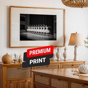 May include: A framed black and white photograph of ballet dancers in white tutus and arm positions. The photograph is displayed above a wooden cabinet with decorative items. The image has a "PREMIUM PRINT" sticker.