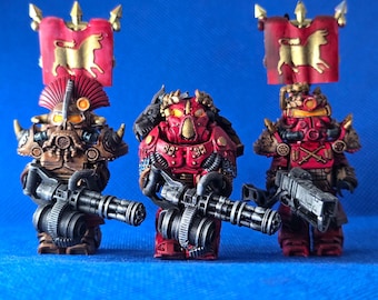 May include: Three miniature warrior figures in red and bronze armor, each holding a large multi-barreled weapon. Two figures feature tall red banners with a gold bull emblem. The figures have detailed helmets, shoulder pads, and mechanical gear.