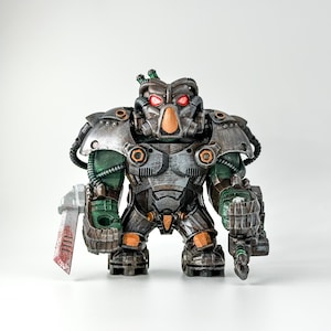 Könnte beinhalten: Ein grünes und silbernes Roboter-Spielzeug mit roten Augen und einem großen, detaillierten Kopf. Der Roboter hält eine große, silberne Klinge in seiner linken Hand und eine kleinere, silberne Waffe in seiner rechten Hand.