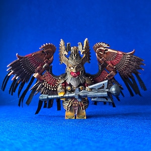 Könnte beinhalten: Eine detaillierte Lego-Figur eines Kriegers mit großen, verzierten Flügeln. Die Figur hat einen goldenen Helm, ein rotes Gesicht und hält einen grauen Streitkolben. Die Flügel sind bronze- und rotfarben, vor blauem Hintergrund.