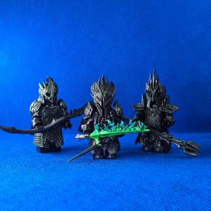 Könnte beinhalten: Drei schwarze und grüne Miniaturfiguren von Kriegern, die Rüstungen tragen und Waffen halten. Die Figuren sind in Kampfstellung.