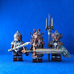 Könnte beinhalten: Drei Lego-Minifiguren von Fantasy-Kriegern mit detaillierter Rüstung und Waffen. Eine Figur hält einen Dreizack, eine andere ein großes Schwert und die dritte ein Schwert und einen Schild. Die Figuren haben Helme und verzierte Designs, vor blauem Hintergrund.