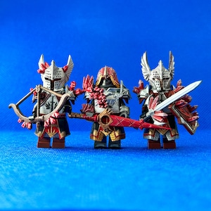 Könnte beinhalten: Drei Miniaturfiguren von Rittern in rot-weißer Rüstung, die Waffen halten. Der Ritter links hält einen Bogen und Pfeil, der Ritter in der Mitte hält ein Schwert, und der Ritter rechts hält ein Schwert und einen Schild.