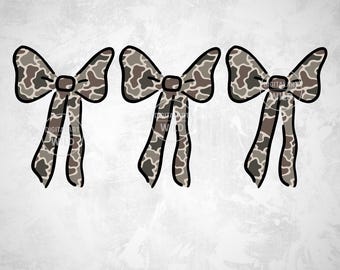 May include: Three decorative bows with a camouflage pattern in shades of brown, gray, and tan. Each bow has a central knot and long, flowing tails. The image includes the text "01 PNG DESIGN" in a pink banner at the bottom.
