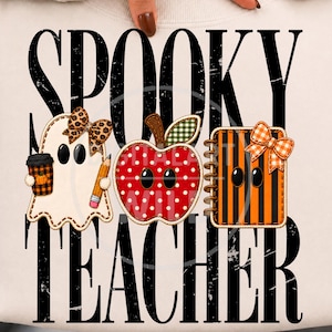 May include: A light-colored sweatshirt featuring the black distressed text SPOOKY TEACHER. The design includes a ghost with a leopard print bow holding a coffee cup and pencil, a red polka-dot apple, and an orange and black striped notebook with a bow.