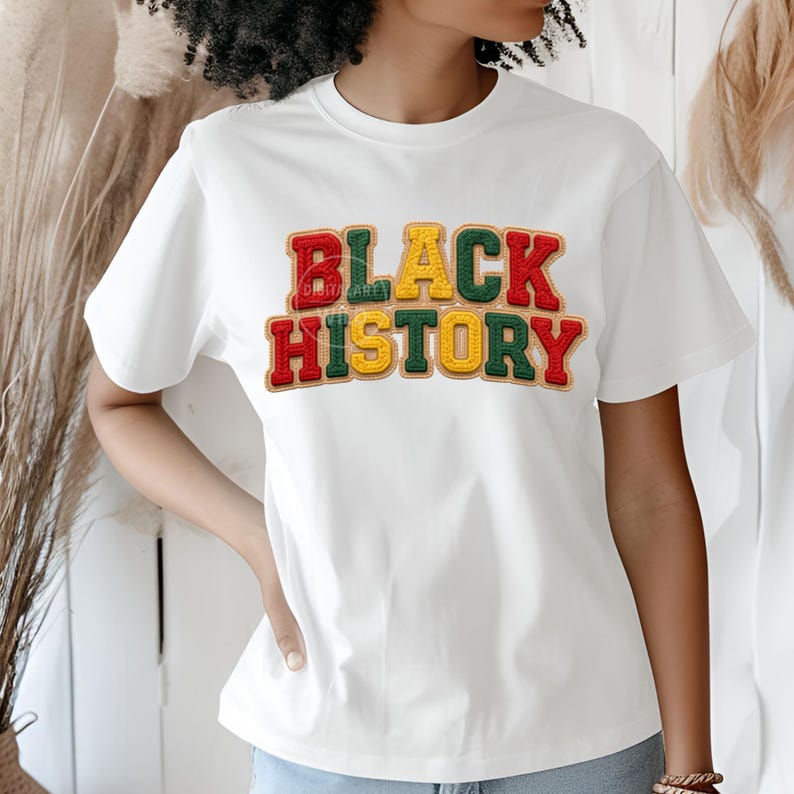 May include: White t-shirt with the words "BLACK HISTORY" in a colorful, textured design. The text is in red, green, and yellow, with a vintage, embroidered look. The shirt has short sleeves and a crew neck.