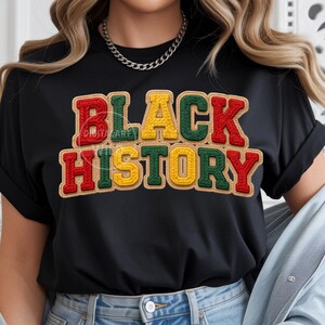 May include: Black t-shirt with the words "BLACK HISTORY" in red, green, and yellow, with a textured, stitched appearance. The text is outlined in a brown color. The shirt has rolled-up sleeves.