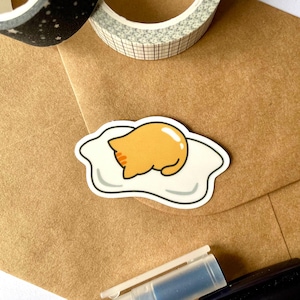 Pegatina de gato con forma de huevo, inspirada en Gudetama, regalo para amantes de los gatos, gato soñoliento, gato perezoso, pegatina de vinilo brillante