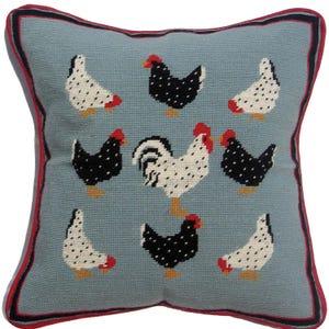 Puede incluir: Cojín cuadrado con fondo azul claro y diseño de punto de aguja de gallinas y un gallo. Las gallinas son negras y blancas con detalles rojos. El cojín tiene un borde rojo y negro.