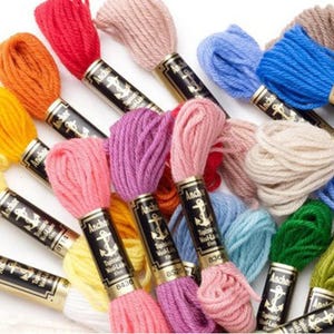 May include: A collection of colorful embroidery floss skeins in shades of red, orange, yellow, pink, purple, blue, green, and cream. Each skein has a black and gold label with an anchor logo.