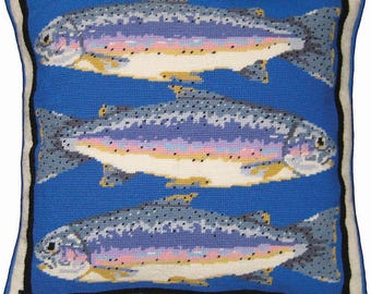 Puede incluir: Un cojín cuadrado de punto de aguja con tres truchas dispuestas horizontalmente sobre un fondo azul brillante. Los peces tienen escamas grises, rosas y blancas con puntos negros. El cojín tiene un borde negro y un remate de color crema.