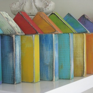Puede incluir: Una fila de casas de madera coloridas pintadas en tonos de azul, verde, amarillo, naranja y morado. Las casas están dispuestas en línea en un estante blanco.