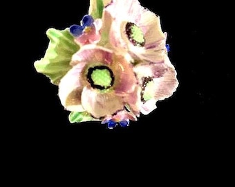 May include: A cluster of three pink flowers with green centers and blue accents. The flowers are arranged in a bouquet and have a delicate, vintage aesthetic.