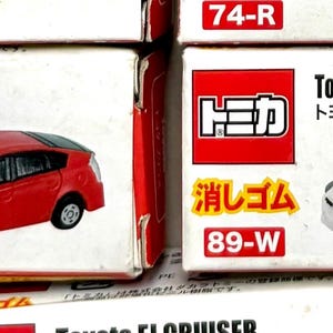 May include: Several toy car boxes are displayed, featuring the Toyota Prius model. The boxes are white and red, with the car's name and Japanese text. One box shows a red Prius, another a white Prius.