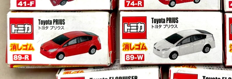 May include: Several toy car boxes are displayed, featuring the Toyota Prius model. The boxes are white and red, with the car's name and Japanese text. One box shows a red Prius, another a white Prius.