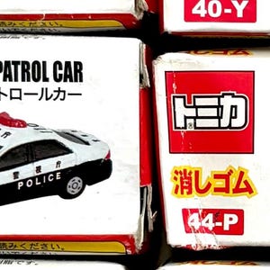 May include: Two toy car boxes. One box features a white and black Toyota Crown Patrol Car with the word "POLICE" on the side. The other box shows a white and black Mazda RX-8 Patrol Car.