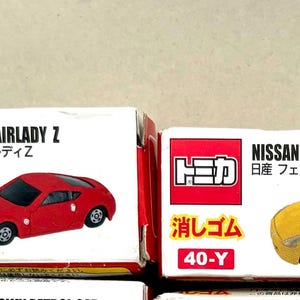 May include: Boxes of toy cars, featuring a red and a yellow Nissan Fairlady Z model. Each box has the car's image, the brand name, and Japanese text. The boxes are white with red accents.