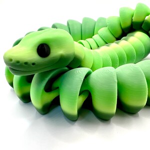 May include: A green and yellow articulated snake toy. The snake's head is a lighter shade of green with a black eye. The body is made of connected segments that allow for flexible movement. The toy is designed to resemble a snake.