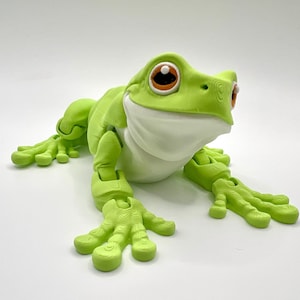 May include: A lime green frog figurine with a white belly and large, expressive eyes. The frog has articulated limbs and a smiling expression, giving it a friendly appearance. The frog is a whimsical decorative item.