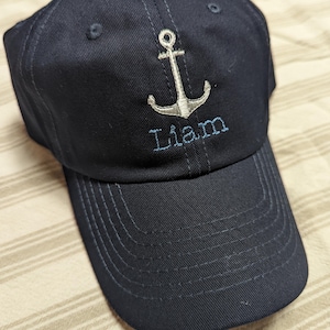 May include: A navy blue baseball cap with a white anchor and the name "Liam" embroidered on the front.