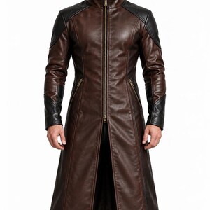 May include: A long brown leather coat featuring black leather panels on the shoulders and sleeves. The coat has a high collar, a full-length central metal zipper, and two slanted zippered pockets at the waist. It is worn with black trousers and boots.