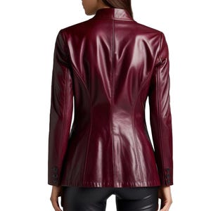 May include: A burgundy leather blazer with a stand-up collar and long sleeves. The back view shows a tailored fit with button details on the cuffs. The jacket is a deep red color.