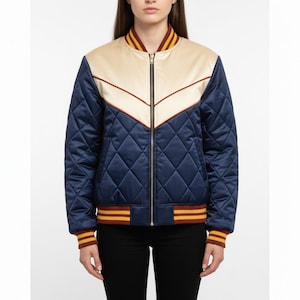 Könnte beinhalten: Eine gesteppte Bomberjacke in Marineblau, Creme und Burgunderrot. Die Jacke hat einen cremefarbenen Einsatz mit einem burgunderfarbenen Chevron-Design, einen marineblauen Körper und bordeauxrot-gold gestreifte Manschetten und Kragen. Die Jacke hat einen durchgehenden Reißverschluss.