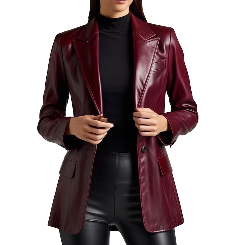 May include: A burgundy leather blazer with a notched lapel, two front pockets, and a single-button closure. The blazer is worn over a black turtleneck and black pants. The jacket has a tailored fit.