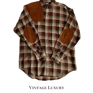 May include: A long-sleeve button-down shirt featuring a brown, cream, and green plaid pattern. The shirt includes a brown suede shoulder patch on the right side and matching brown suede elbow patches on both sleeves, with a single chest pocket.