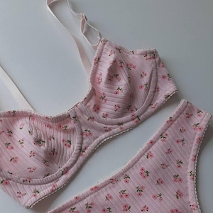 May include: A pink floral lingerie set with a bra and matching thong. The bra has adjustable straps and a delicate lace trim. The thong has a low-rise cut and a lace trim.