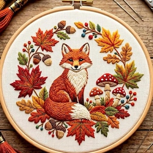 Peut inclure: Un tambour à broder circulaire en bois contenant un panneau en tissu avec un motif de point d'aiguille détaillé représentant un renard orange central entouré d'une couronne de feuilles d'érable, de feuilles de chêne, de glands et de champignons.