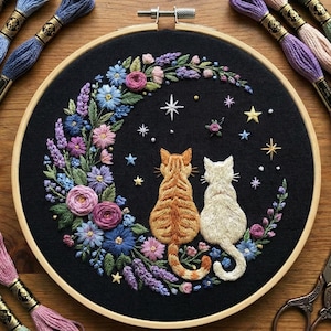 以下が含まれることがあります： 黒い背景に星を眺める2匹の猫が刺繍された作品。青、ピンク、紫、緑の色合いの花々が三日月型に猫を囲んでいます。木製のフレームに収められた、手作りの温かみのある装飾品です。