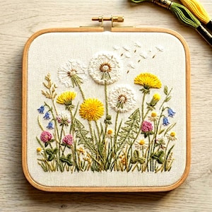 May include: A square embroidery hoop featuring a detailed floral design. The artwork showcases yellow dandelions, white seed heads, pink clover, and bluebells, all meticulously stitched on a cream-colored fabric. The wooden hoop adds a natural touch.