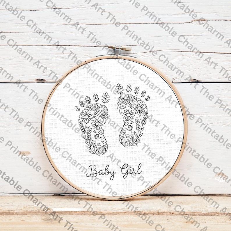 May include: A round embroidery hoop with a white fabric featuring a floral design of baby footprints. The footprints are filled with flowers and leaves. The words "Baby Girl" are written below the footprints in a script font.