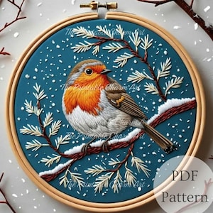 Könnte beinhalten: Detaillierte Stickerei eines Rotkehlchens auf einem schneebedeckten Ast, vor einem tealblauen Hintergrund mit fallendem Schnee. Der Vogel hat orange und weiße Federn mit braunen Flügeln. Die Stickerei ist in einem Holzreifen gerahmt. Der Text auf dem Bild lautet "The Printable Charm Art" und "PDF Pattern".