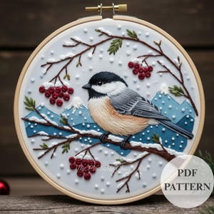 May include: Embroidered hoop art featuring a chickadee bird perched on a branch with red berries and snow-covered branches. The background includes blue mountains and falling snow. The text "PDF PATTERN" is visible.