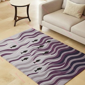 Puede incluir: Una alfombra rectangular con un diseño de olas en tonos grises y morados. Siluetas de peces negros están dispersas por la alfombra, que está colocada sobre un suelo de baldosas claras. Un sofá y una mesa auxiliar están en el fondo.