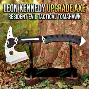 Könnte beinhalten: Eine schwarze und silberne taktische Tomahawk-Axt mit dem Text "LEON KENNEDY UPGRADE AXE" und "RESIDENT EVIL TACTICAL TOMAHAWK". Die Axt wird auf einem schwarzen Ständer vor einem Baumstamm ausgestellt. Die Axt hat einen schwarzen Griff und eine silberne Klinge.