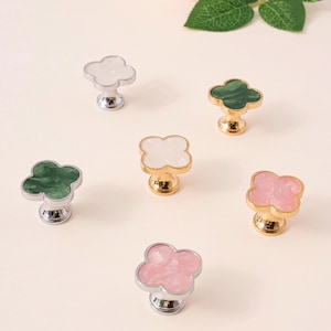 May include: Six decorative clover-shaped cabinet knobs in various colors, including white, pink, and green. The knobs have metallic bases in silver and gold. The text "PrprfctnTreasures" is at the top.
