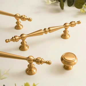 May include: Gold-toned cabinet hardware set, including handles and a knob. The handles have a detailed, ornate design with a classic aesthetic. The text "PrprfctnTreasures" is visible at the top of the image.