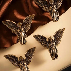 May include: Four bronze-colored angel figurines with outstretched wings. Each angel is depicted in a praying pose, with detailed feathering on the wings. The text "Prprtn Treasures" is visible at the top.
