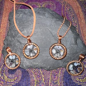 May include: Three copper wire wrapped pendants with a variety of small stones and crystals encased in clear resin. The pendants are on a dark gray background.