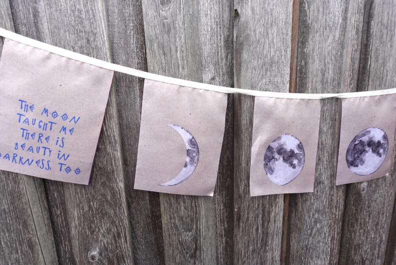 K&ouml;nnte beinhalten: Ein braunes Papierbanner mit dem Text "The moon taught me there is beauty in darkness, too." und vier Illustrationen des Mondes in verschiedenen Phasen.