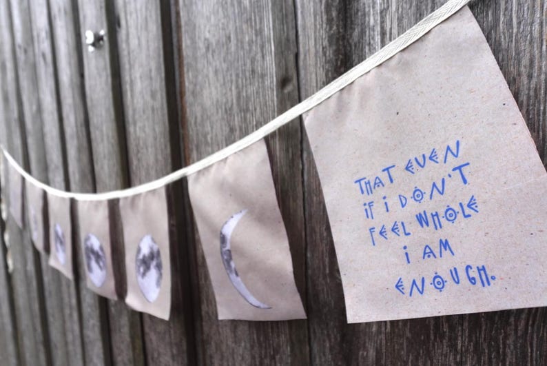K&ouml;nnte beinhalten: Ein Banner mit wei&szlig;em Hintergrund und blauem Text, der "That even if I don't feel whole I am enough." lautet. Das Banner h&auml;ngt an einem Holzzaun.