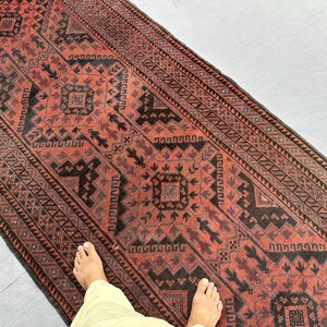 Pode incluir: Um tapete retangular com um design vermelho e preto. O tapete apresenta um padrão geométrico com um medalhão central. A borda do tapete tem um padrão repetitivo. O tapete é provavelmente feito de lã e é adequado para um corredor ou entrada.