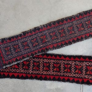 Op de afbeelding: Twee smalle, rechthoekige, geweven tapijten met geometrische patronen. De tapijten hebben een kleurenpalet van rood, zwart en blauw. De tapijten worden waarschijnlijk gebruikt als decoratieve lopers of accenten.